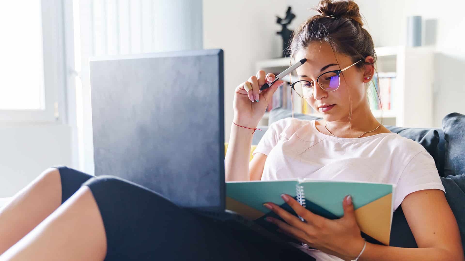 woman holds pen to forehead and concentrates on her online studies