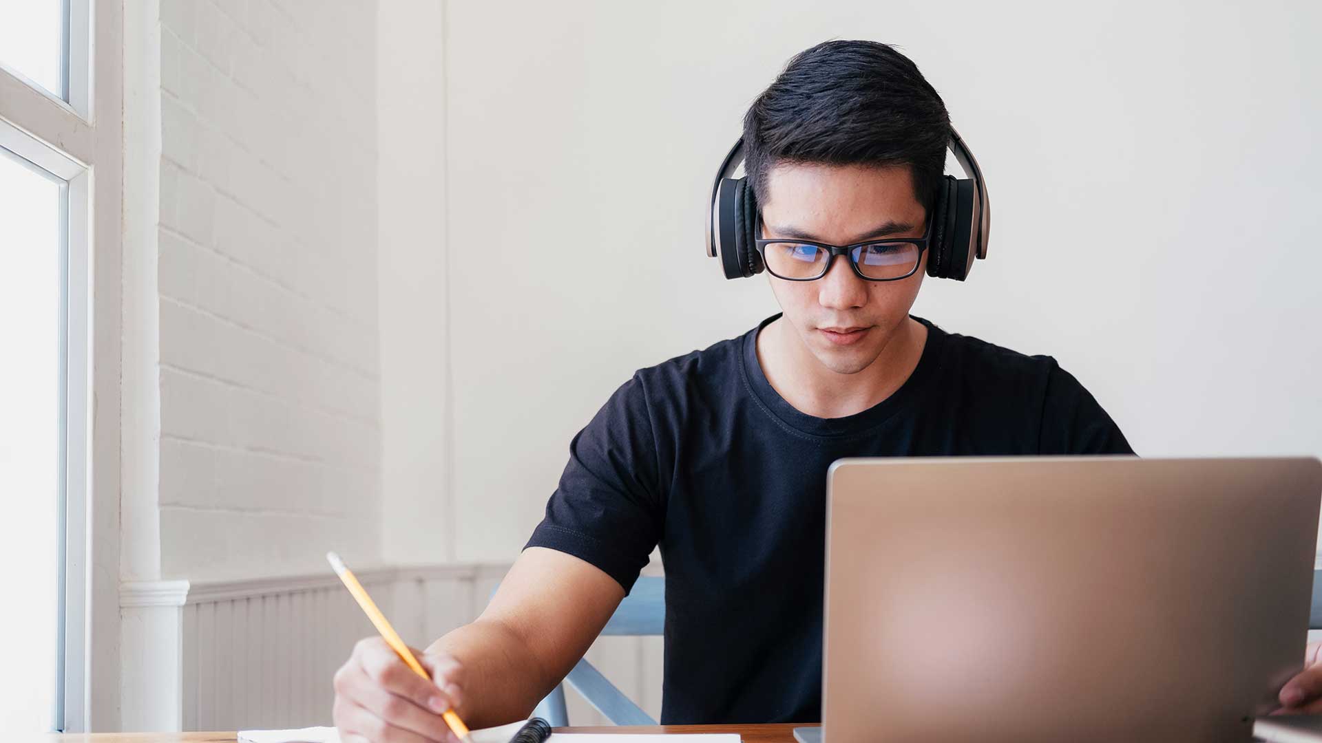 male student with headphones studying online course and taking notes